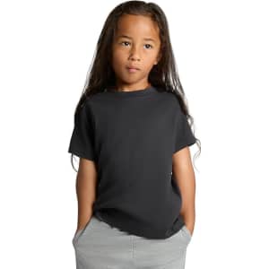 A black kids' heavy faded tee with short sleeves, worn by a child with long hair, standing with hands in pockets.