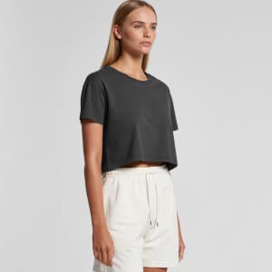 A woman models a dark grey cropped T-shirt, paired with light-coloured shorts. The shirt has a simple design and logo.