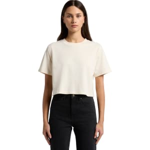 A cropped, short-sleeve t-shirt in a light cream colour, displayed on a model wearing black jeans. The shirt features a logo.