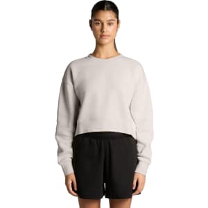 A cropped, light grey jumper with a relaxed fit, paired with black shorts. The model stands with arms by her side.