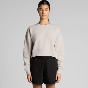 A light grey cropped jumper is displayed, paired with black shorts. The jumper has a relaxed fit and features a branding logo.