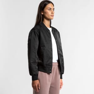 A black varsity bomber jacket worn by a model, featuring a front snap closure and ribbed cuffs.