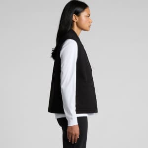 A black canvas heavy vest features a simple design with side pockets and a logo. Model wears a white shirt underneath.