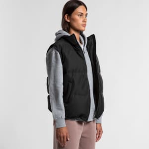 A woman wearing a black puffer vest over a grey hoodie, showcasing a casual layered style. The vest features a logo.