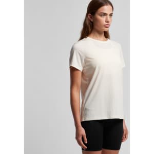 A woman wearing a light cream-coloured t-shirt with short sleeves, paired with black shorts. The shirt has a logo.