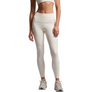 A pair of cream-coloured active leggings featuring a high waistband, modelled with a matching crop top and trainers.