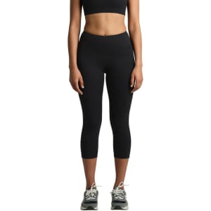 A pair of black mid-length leggings, featuring a fitted design and a subtle logo, worn with athletic shoes.