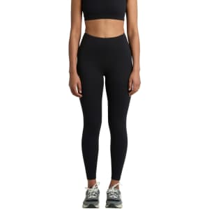 Black seamless leggings displayed on a model, paired with a matching crop top and athletic shoes. The image features branding.