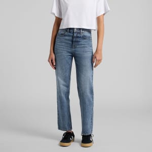Straight jeans in a light blue wash, styled with a white crop top and black sneakers. The jeans have a subtle logo detail.
