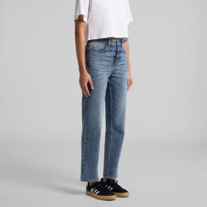 Light blue straight jeans displayed on a model, paired with a white crop top and black sneakers. The image features a logo.
