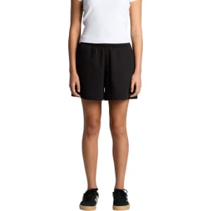 Black track shorts with a relaxed fit, featuring an elastic waistband and side pockets. Model is standing.
