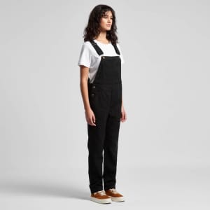 Black canvas overalls featured on a model, paired with a white t-shirt and brown shoes. The overalls have a logo detail.