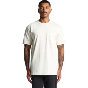 A light cream-coloured pocket t-shirt displayed on a model with tattoos, featuring a simple design and logo.