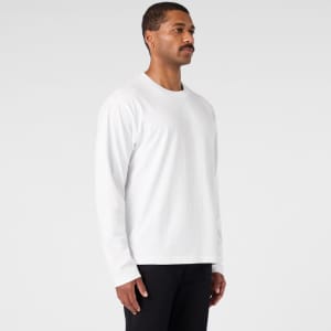 A white long-sleeve T-shirt is displayed on a model standing sideways, paired with black pants. The shirt has a logo.