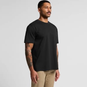 A black t-shirt featuring a classic design and a logo, worn by a man with tattoos, standing against a plain background.