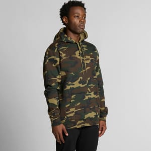 A man wearing a green and brown camouflage hoodie with a front pocket and drawstring hood, featuring a logo.