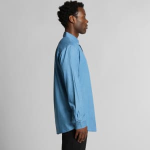 A blue denim button-up shirt displayed on a model from the side, featuring long sleeves and a collar.