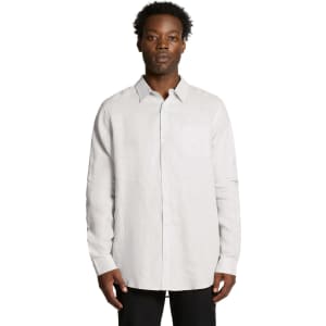A button-up linen shirt in light grey, featuring long sleeves and a chest pocket. The model stands facing forward.