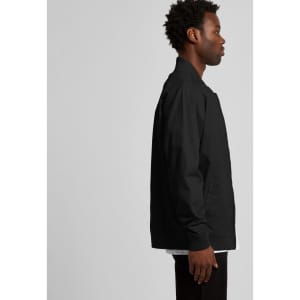 A man in a black bomber jacket stands sideways, showcasing the jacket's design and fit. The jacket has a logo.