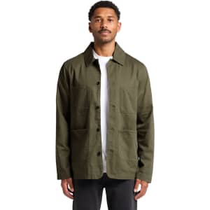 A man wearing an olive green Chore Jacket with multiple pockets and a logo. The jacket has a classic collar and button front.