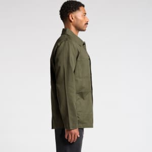 A man wearing an olive green canvas chore jacket, viewed from the side, with a simple design and a logo present.