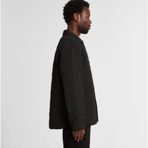 A black quilted puffer jacket viewed from the side, featuring a button-down front and a subtle logo.