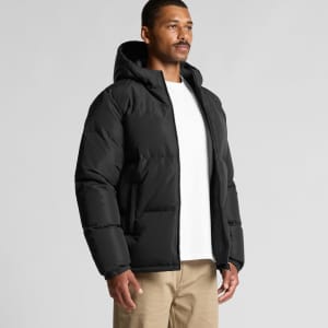 A man in a black hooded puffer jacket stands against a plain background. The jacket features a hood and zipper closure.