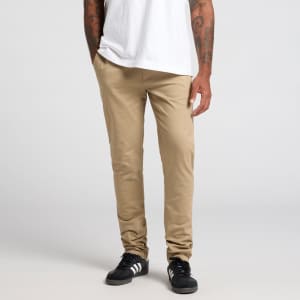 Beige pants are displayed on a model standing with hands in pockets, wearing a white t-shirt and black shoes.