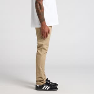 A pair of khaki standard pants displayed on a model, paired with black shoes and a white shirt.