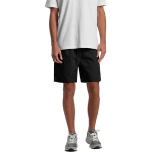 A pair of black sports shorts with an elastic waistband, featured on a model wearing a white T-shirt and grey shoes.
