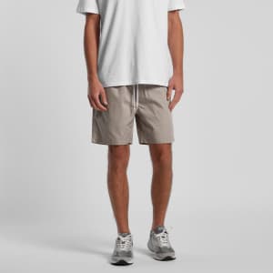 A pair of beige beach shorts, 17 inches long, worn with a white t-shirt and grey sneakers. The shorts feature a drawstring.
