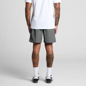 A person wearing grey swim shorts, viewed from the back, with visible tattoos on their legs.