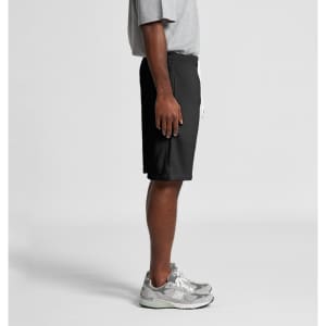 A pair of black sports shorts with a drawstring waist, shown on a model from the side. The model is wearing grey sneakers.