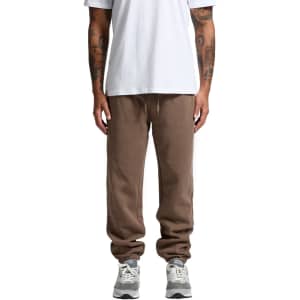 Brown track pants with an elasticated waistband, featuring a relaxed fit and a logo on the side, paired with grey sneakers.