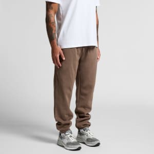 A pair of brown track pants with a relaxed fit, paired with light grey sneakers. The model is wearing a plain white t-shirt.