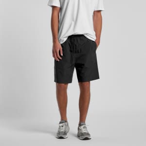 Black sports shorts with an elastic waistband, modelled by a person wearing a white t-shirt and grey sneakers.