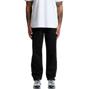 Black relaxed pants worn by a person standing, paired with a plain white t-shirt and athletic shoes.