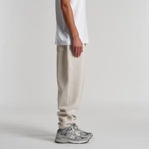 A pair of cream track pants with a relaxed fit, featuring a side pocket and worn with grey sneakers.