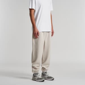 A person wearing beige track pants paired with a white t-shirt and grey sneakers, with the pants featuring a logo.