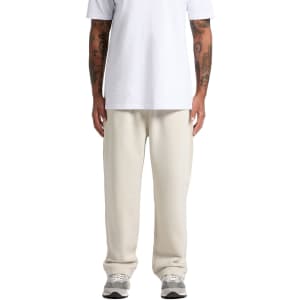A person stands in relaxed cream track pants paired with a white t-shirt. The pants have a logo detail.