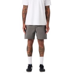 A pair of grey dress shorts worn by a person with tattoos, standing in a casual outfit.