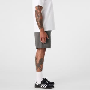 A person stands in profile wearing faded grey dress shorts and a white t-shirt, paired with black shoes and socks.