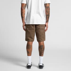 Canvas shorts in a light brown hue with cargo pockets, viewed from the back on a person wearing a white T-shirt.