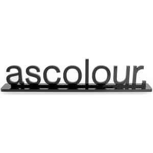 A black acrylic display featuring the word "ascolour" in bold, stylised letters, mounted on a flat base.