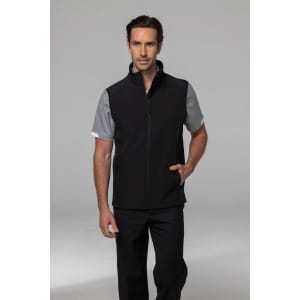 A man wearing a black vest over a grey shirt, posed with hands in pockets against a neutral background.