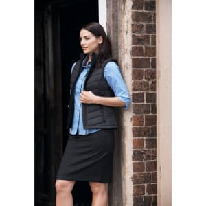 A stylish black quilted vest paired with a blue shirt and black skirt, set against a rustic brick background.
