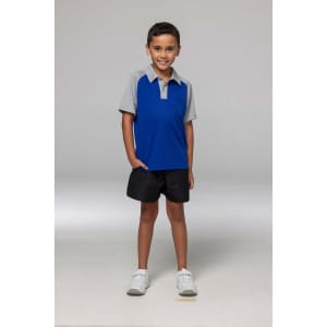 A boy stands confidently in a blue and grey polo shirt paired with black shorts and white shoes.