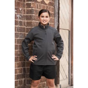 A child wearing a grey jacket stands confidently against a brick wall, paired with black shorts.