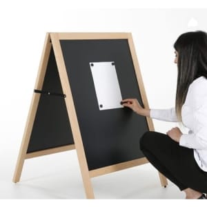 A magnetic black chalkboard A-frame with a wooden frame, being used by a person to attach a note.