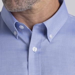 A close-up of a men's button-up shirt in light blue, featuring a pointed collar and buttons. It has a branding logo.